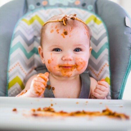 siedzący w krzesełku zadowolony ubrudzony jedzeniem niemowlak