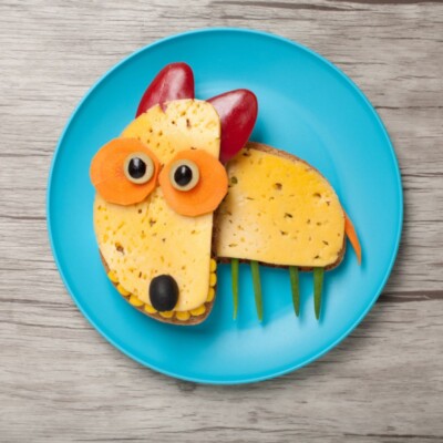 kanapka dla dziecka z sera i warzyw w kształcie pieska leżąca na niebieskim talerzu