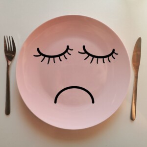 pusty talerz z narysowaną smutną buzią, obok talerza leżą złote sztućce